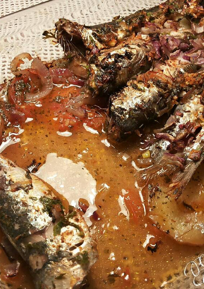Una foto de Sardinas marinadas al horno, con fondo de tomates, cebollas, y patatas asadas