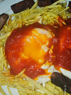 Una foto de Huevos fritos con patatas paja, salsa de tomate y salchichas