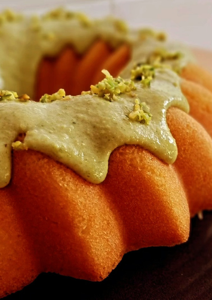 Una foto de Bundt cake genovés de coco con cobertura de crema de pistachos y chocolate blanco (sin gluten)