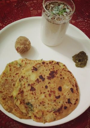 A picture of Aloo paratha with buttermilk and dry fruit ladoo.