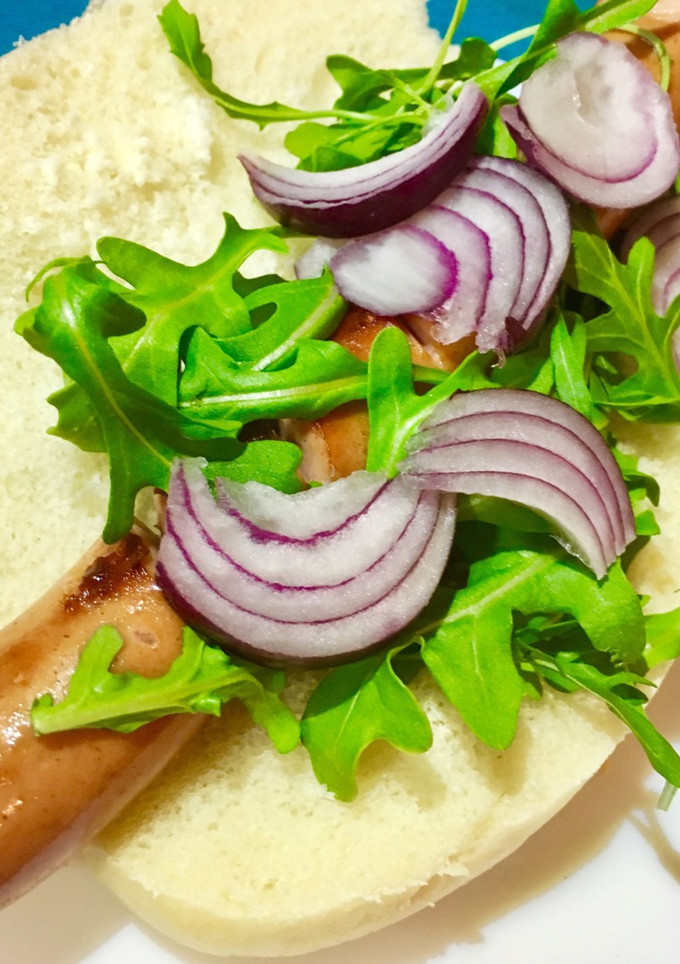 Una foto de Perrito caliente con rúcula, cebolla y salsa barbacoa picante