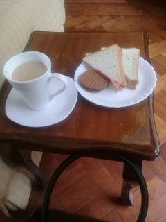 A picture of Cup of tea, slice of buttered n jam bread n a chocolate cookie.