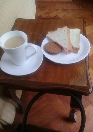 A picture of Cup of tea, slice of buttered n jam bread n a chocolate cookie.