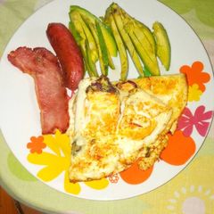 A picture of Fried eggs with sausages and avacado pear.