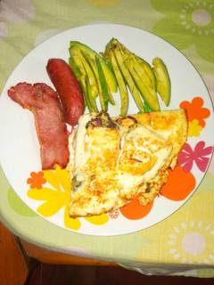 A picture of Fried eggs with sausages and avacado pear.
