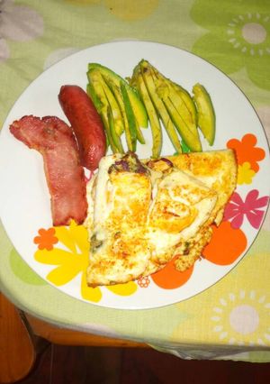A picture of Fried eggs with sausages and avacado pear.