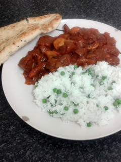 A picture of spicy chicken curry, nan bread with rice & peas.