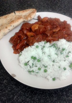 A picture of spicy chicken curry, nan bread with rice & peas.
