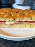 Focaccia bread with Mortadella, grilled tomatoes, melted mozzarella and cornichons