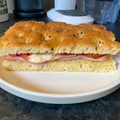 A picture of Focaccia bread with Mortadella, grilled tomatoes, melted mozzarella and cornichons.