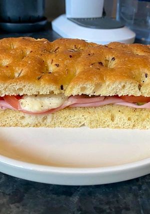 A picture of Focaccia bread with Mortadella, grilled tomatoes, melted mozzarella and cornichons.