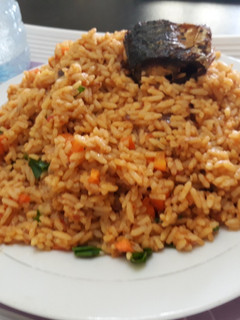 A picture of Jollof rice with carrots and green peas with fish.