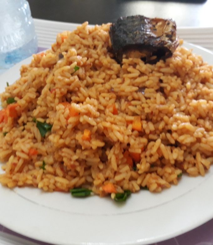 A picture of Jollof rice with carrots and green peas with fish.
