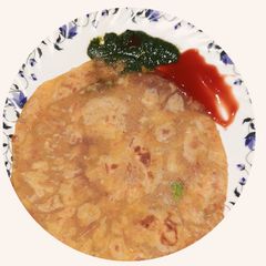 A picture of Spicy vej paratha with red and green chutney.