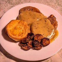 A picture of Fried pork chop in cognac gravy sauce with Yorkshire pudding and Baked Brussel Sprouts.