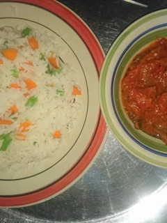 A picture of White rice with carrots and green peas with tomato sauce.