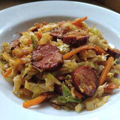 A picture of Sautéed cabbage and carrot with sausage.