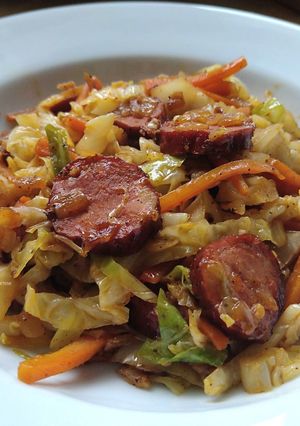 A picture of Sautéed cabbage and carrot with sausage.