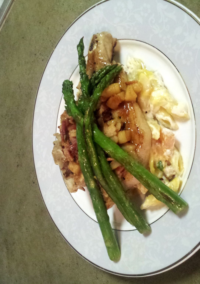 A picture of Bacon Apple Porkchops over loaded mac-n-cheese with Asparagus.