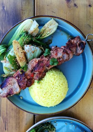 A picture of Asian style pork kebabs, steamed veg and yellow rice.