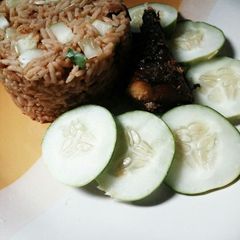 A picture of Turmeric jollof rice with cucumber and fried fish.