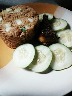 A picture of Turmeric jollof rice with cucumber and fried fish.