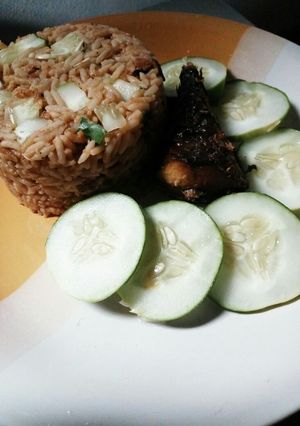 A picture of Turmeric jollof rice with cucumber and fried fish.