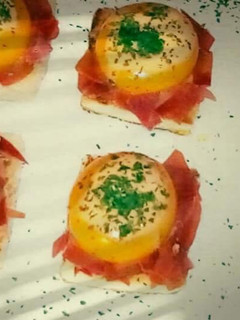 Una foto de Yemas de huevos rellenas de crema de tomate sobre un lecho de jamón ibérico