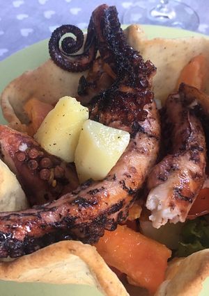 A picture of Marinated and Grilled Octopus with Mixed Salad, Potatoes, Avocado, and Almonds in a Breadstick Basket.