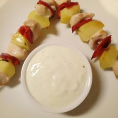 A picture of Chicken and vegetable skewers with tzatziki sauce.