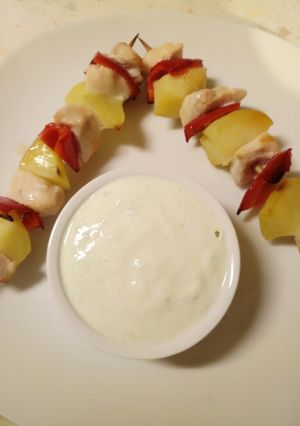 A picture of Chicken and vegetable skewers with tzatziki sauce.
