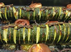 Una foto de Calabacines Hasselback con Panceta y Gouda sobre Lecho de Tomate y Cebolla