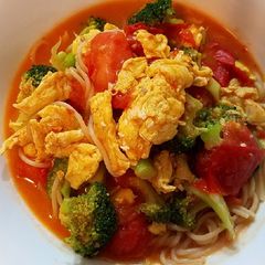 A picture of Scrambled eggs, broccoli and tomatoes over pasta.