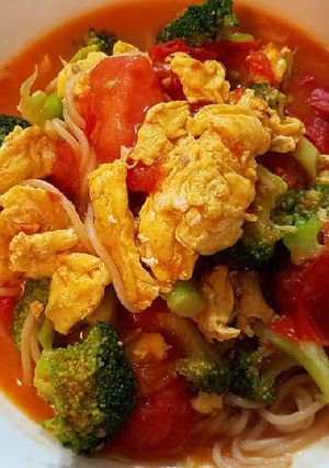 A picture of Scrambled eggs, broccoli and tomatoes over pasta.