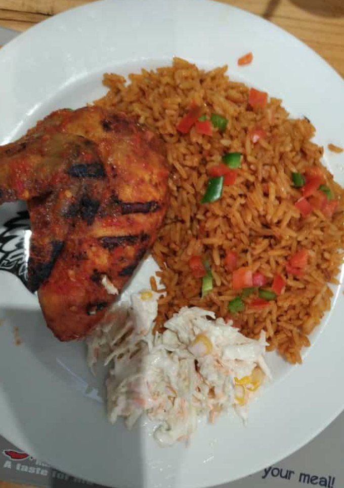 A picture of Jollof rice with coleslaw and fried chicken.
