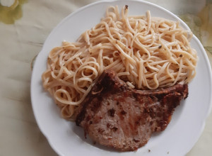 Una foto de Chuleta de Cerdo con Tallarines y acompañada de Tomate al Comino