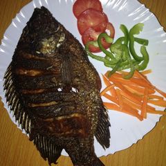 A picture of Deep fried fish garnished with green pepper, carrots and tomatoes.