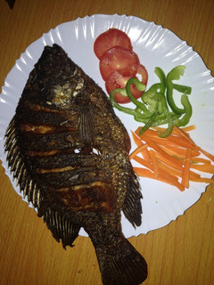 A picture of Deep fried fish garnished with green pepper, carrots and tomatoes.
