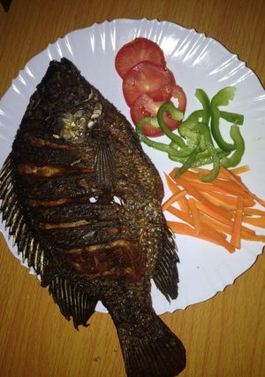 A picture of Deep fried fish garnished with green pepper, carrots and tomatoes.