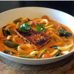 A picture of Thai Coconut Red Curry Soup with Udon Noodles, Carrots, Green Bell Pepper, Bok Choy & Blackened Tofu.