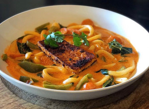 A picture of Thai Coconut Red Curry Soup with Udon Noodles, Carrots, Green Bell Pepper, Bok Choy & Blackened Tofu.
