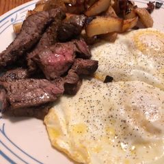 A picture of Steak and eggs with a side of home fries.