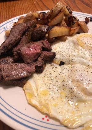 A picture of Steak and eggs with a side of home fries.