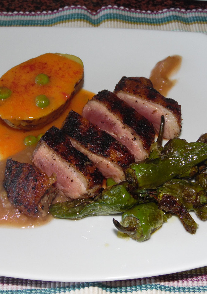 Una foto de Pechuga de pato asada con pimientos del padrón, papa con salsa de carne guisantes y puré de manzana