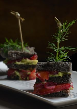 Une photo de Club sandwich pain à l'encre de seiche, avocat et saumon gravlax à la betterave