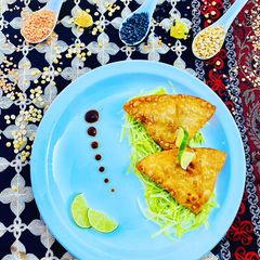 A picture of Homemade Fresh Samosa served on bed of lettuce with tamarind sauce and limes.