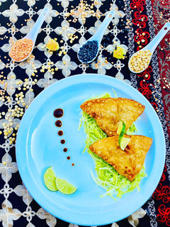 A picture of Homemade Fresh Samosa served on bed of lettuce with tamarind sauce and limes.