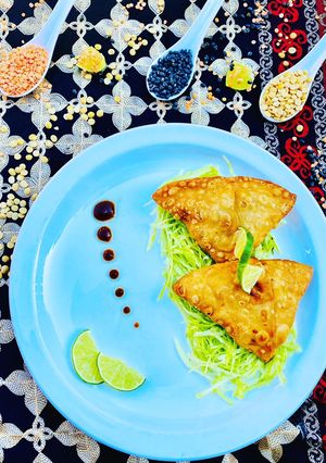 A picture of Homemade Fresh Samosa served on bed of lettuce with tamarind sauce and limes.
