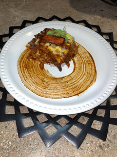 Una foto de Lasaña de mole coloradito con pollo y frituras de plátano macho