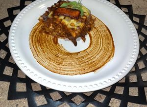 Una foto de Lasaña de mole coloradito con pollo y frituras de plátano macho
